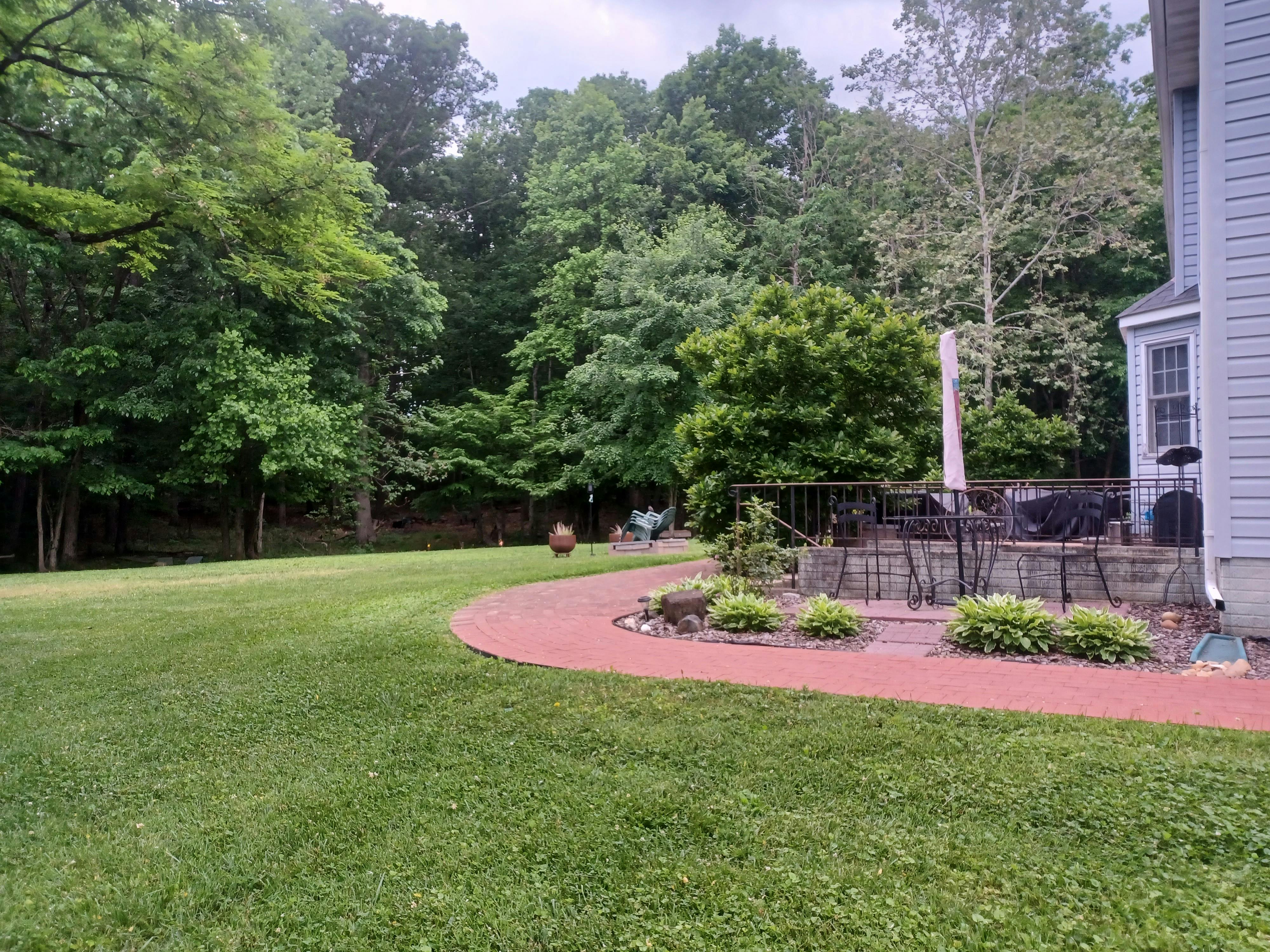 Green lawn next to a curved red brick path leading to a patio with outdoor furniture