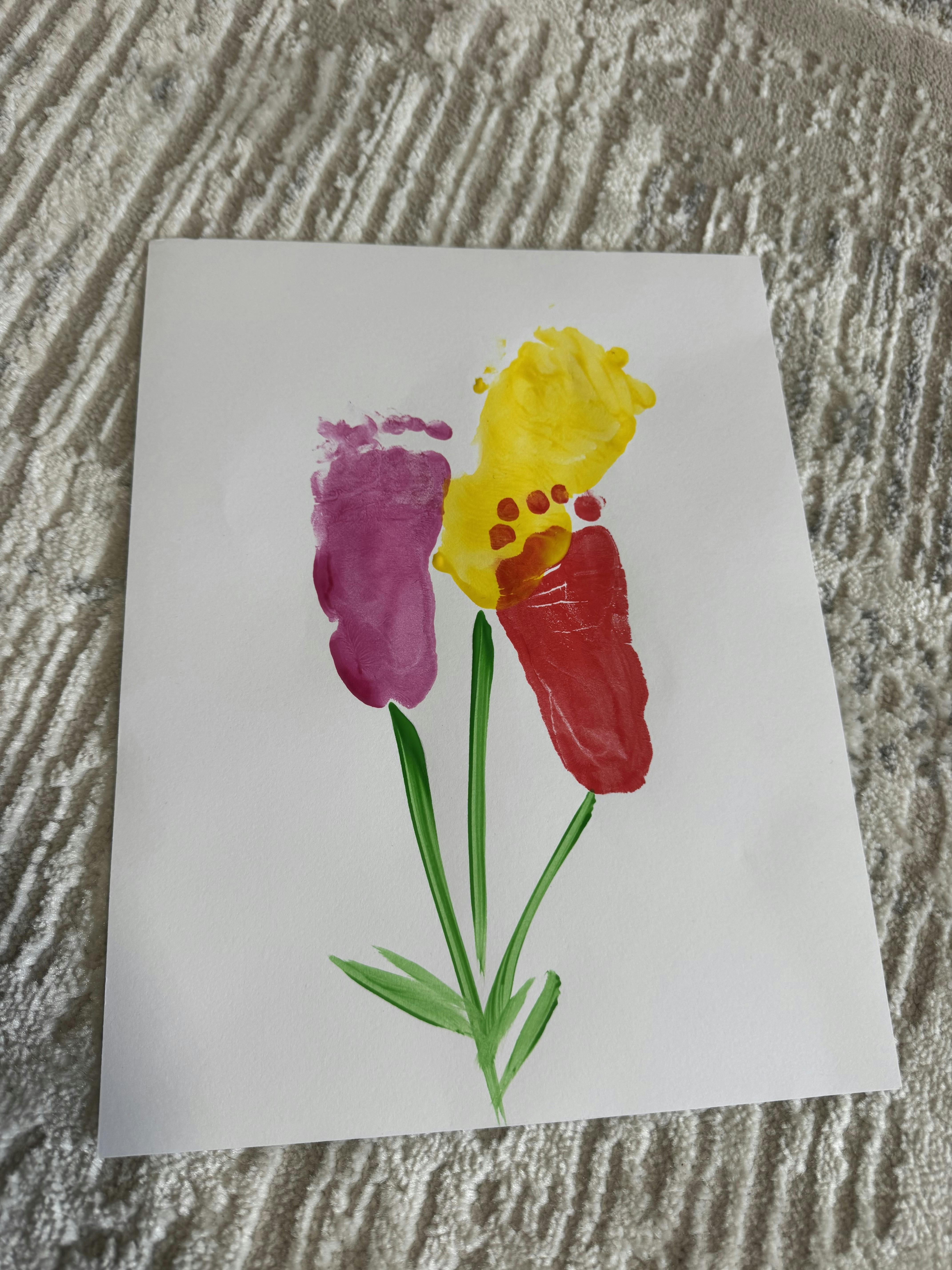 Baby footprints in purple, yellow, and red paint arranged like flowers on a white paper