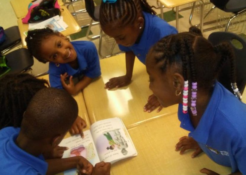 Four children in blue shirts looking at a book on a table