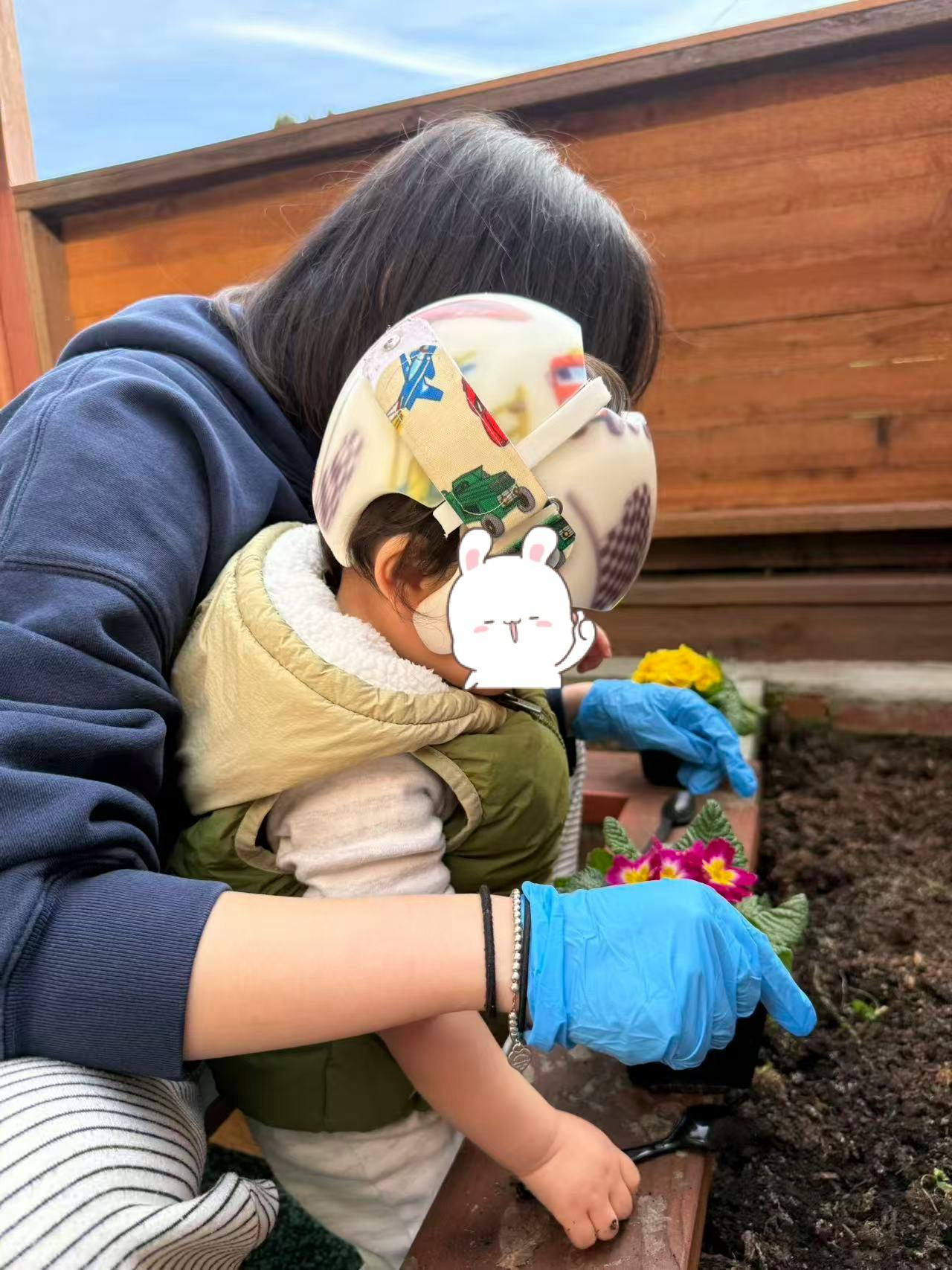 Person in blue gloves and child planting flowers together in a garden