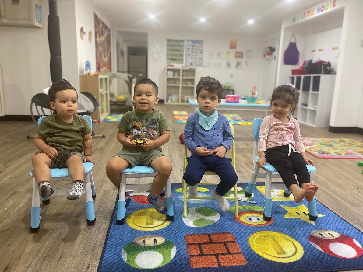 Four children sitting on small chairs in a classroom