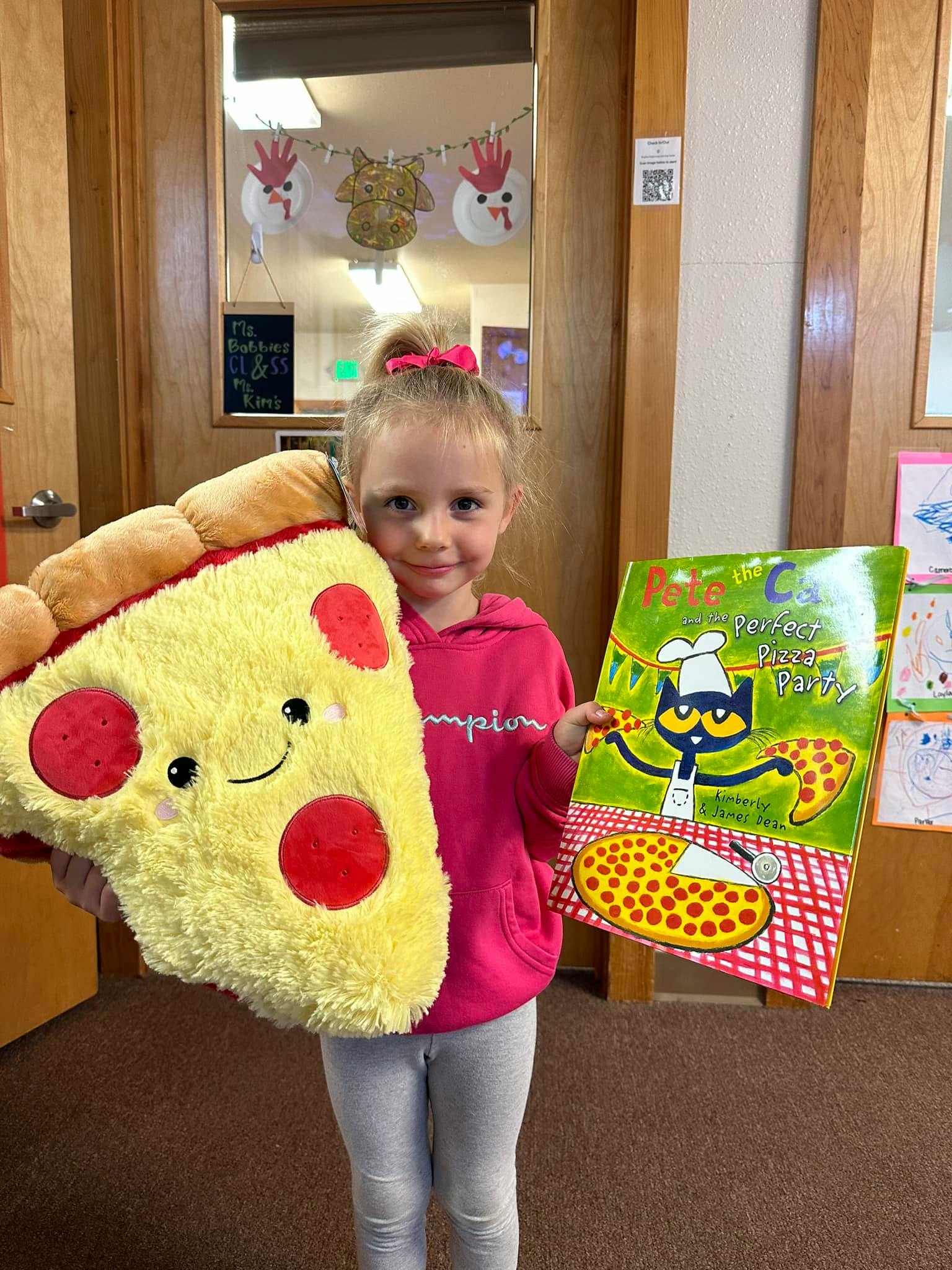 Child holding a pizza slice plushie and a book titled "Pete the Cat Perfect Pizza Party"