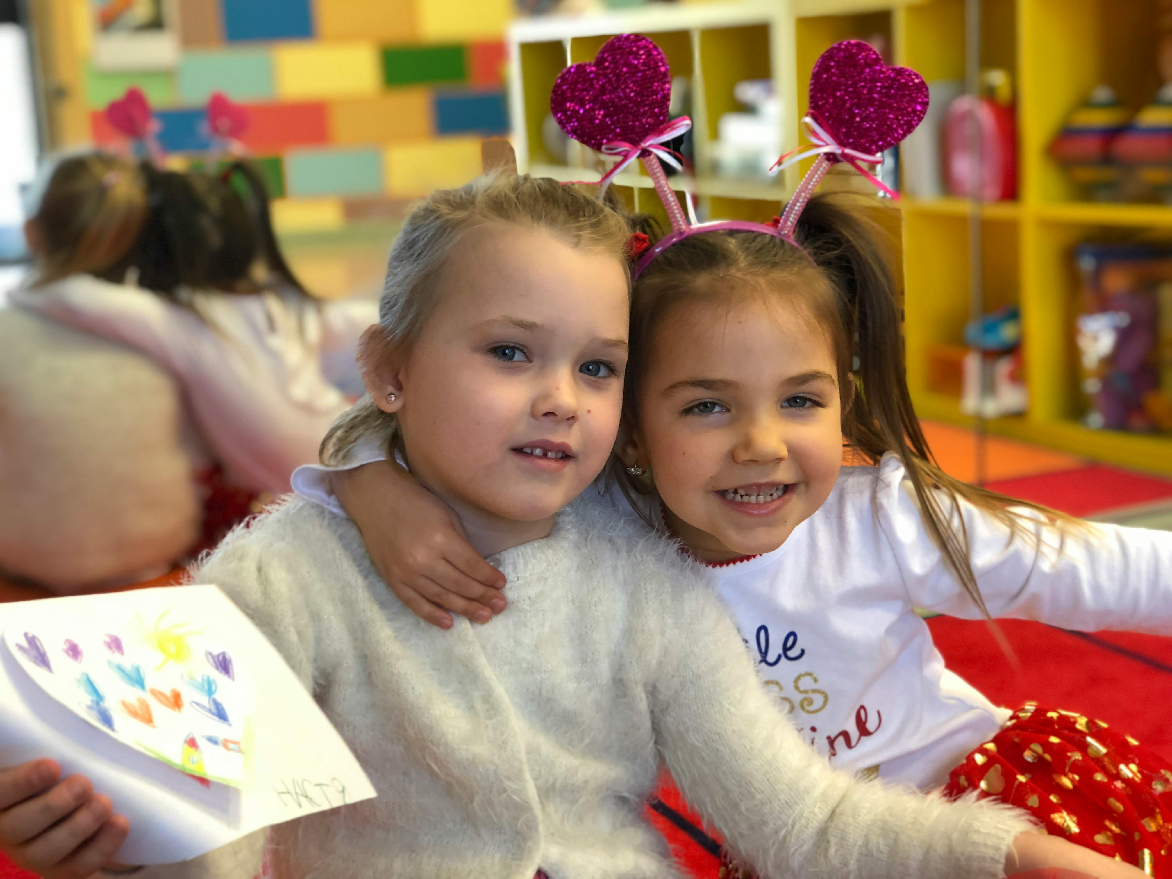 Two children with one holding a drawing and the other wearing a heart headband