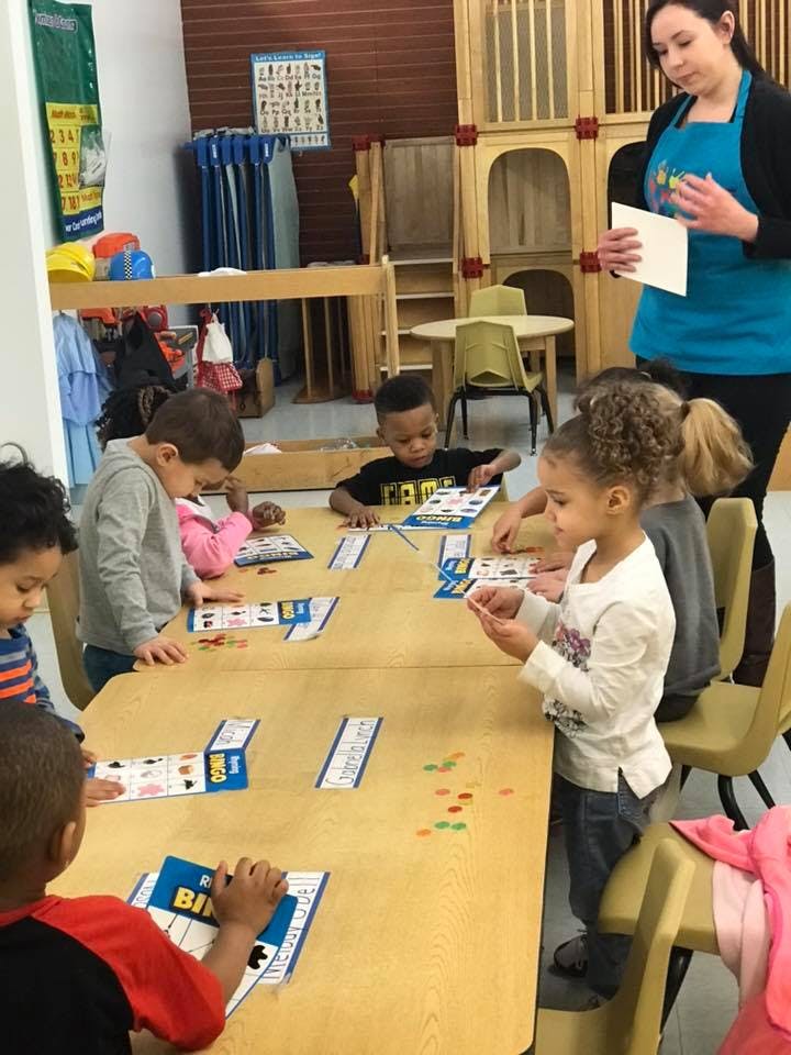 Adult and children playing a game at a table in a classroom