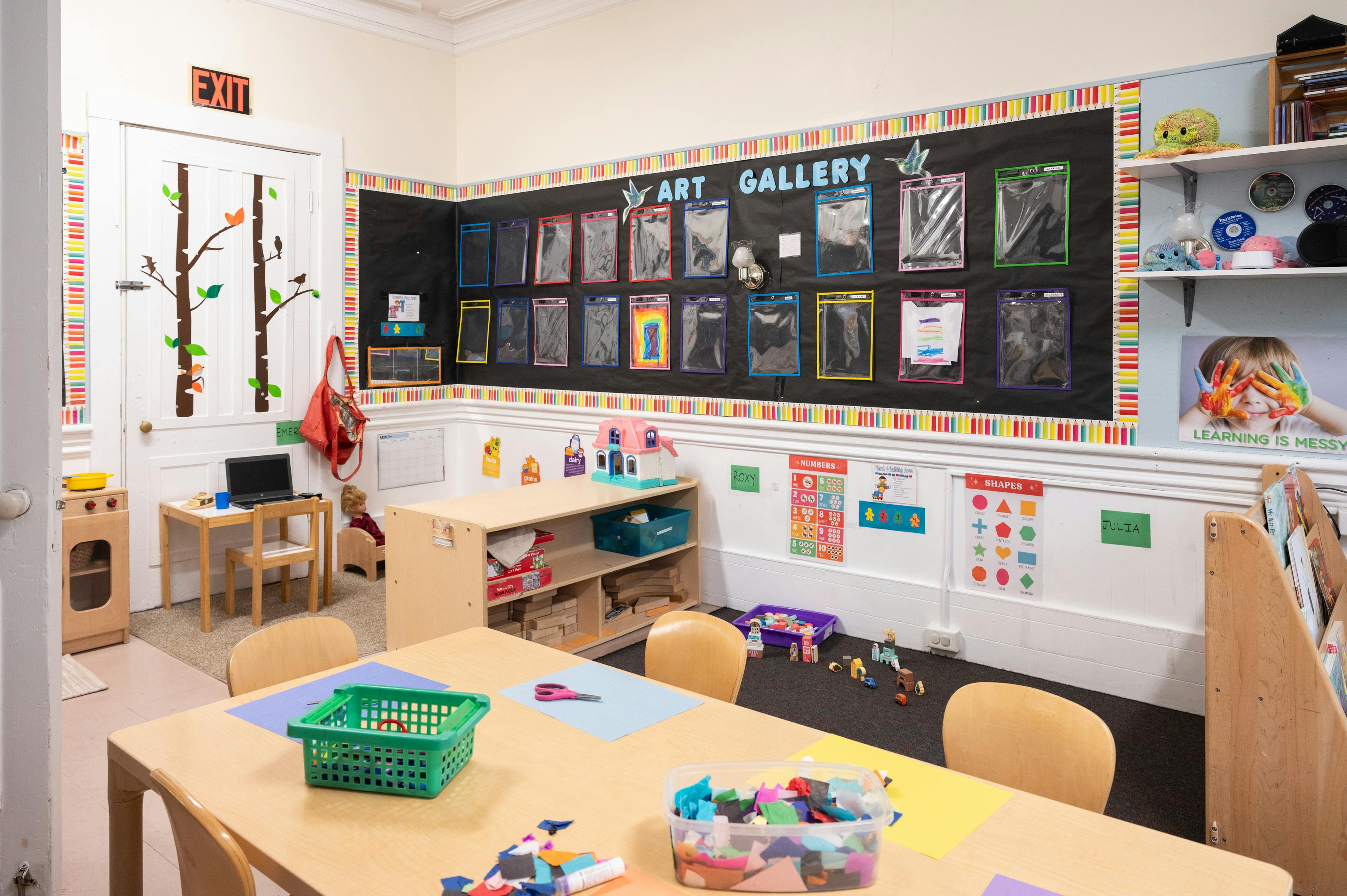 Classroom with tables, storage shelves, and an art gallery display on the wall