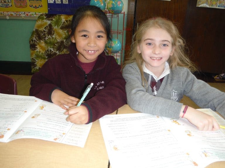 Two children writing at a desk in a classroom