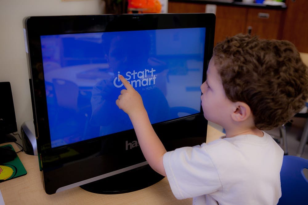 Child pointing at a computer screen displaying "Start Smart"