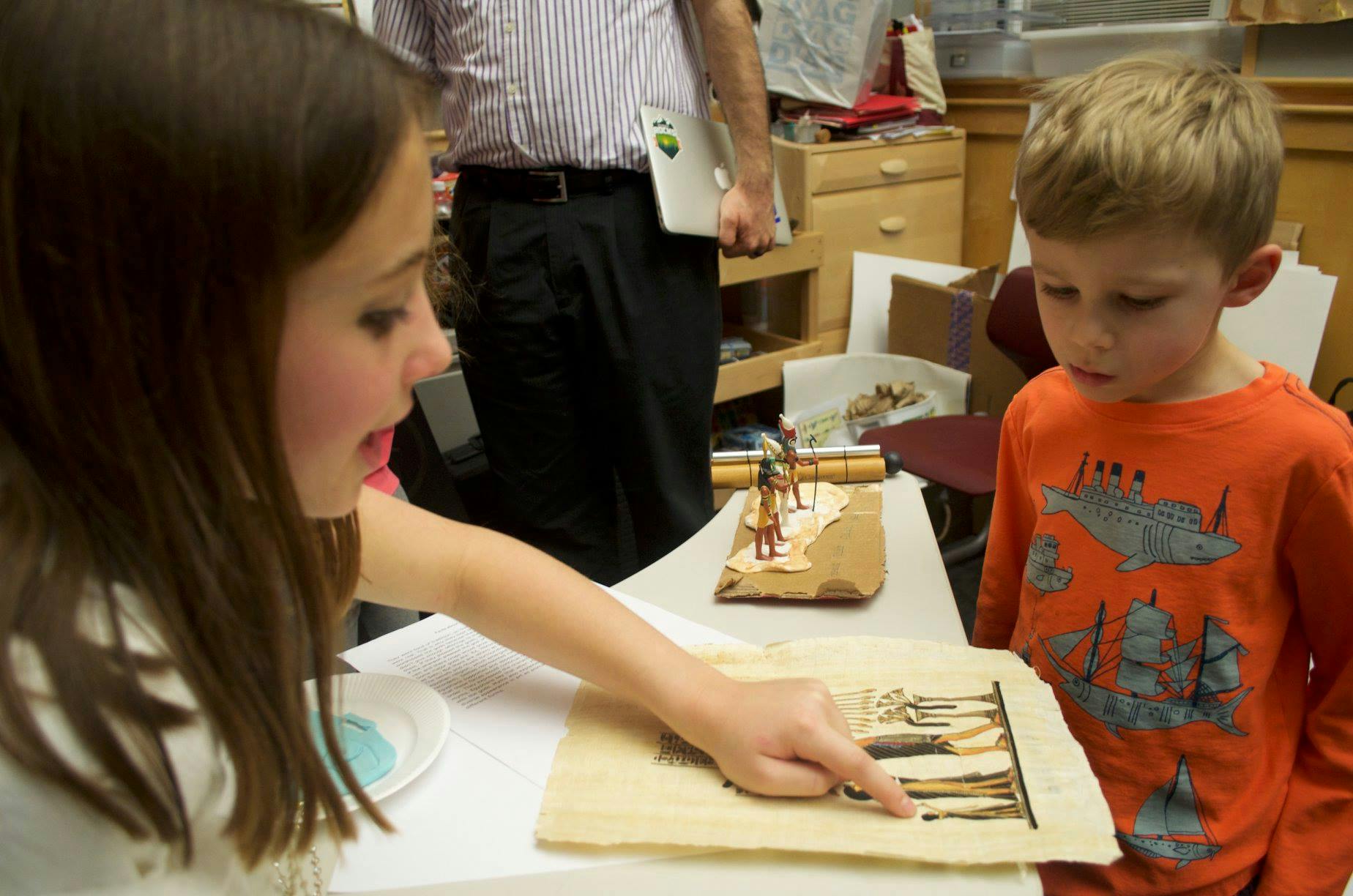 Teen pointing at a drawing on a table with a child looking on the child looking on the child looking on