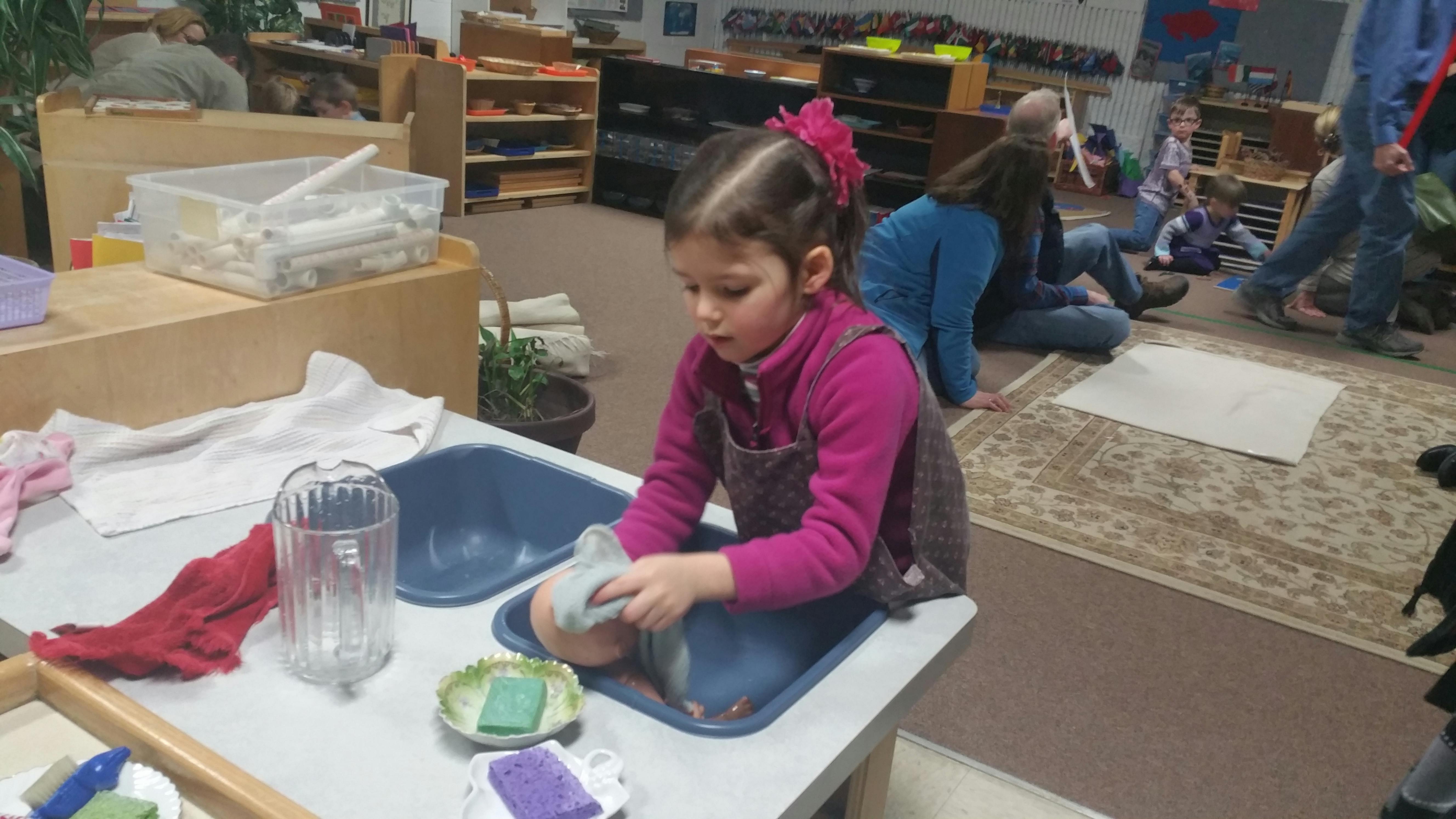 Child washing an object in a basin on a table in a classroom