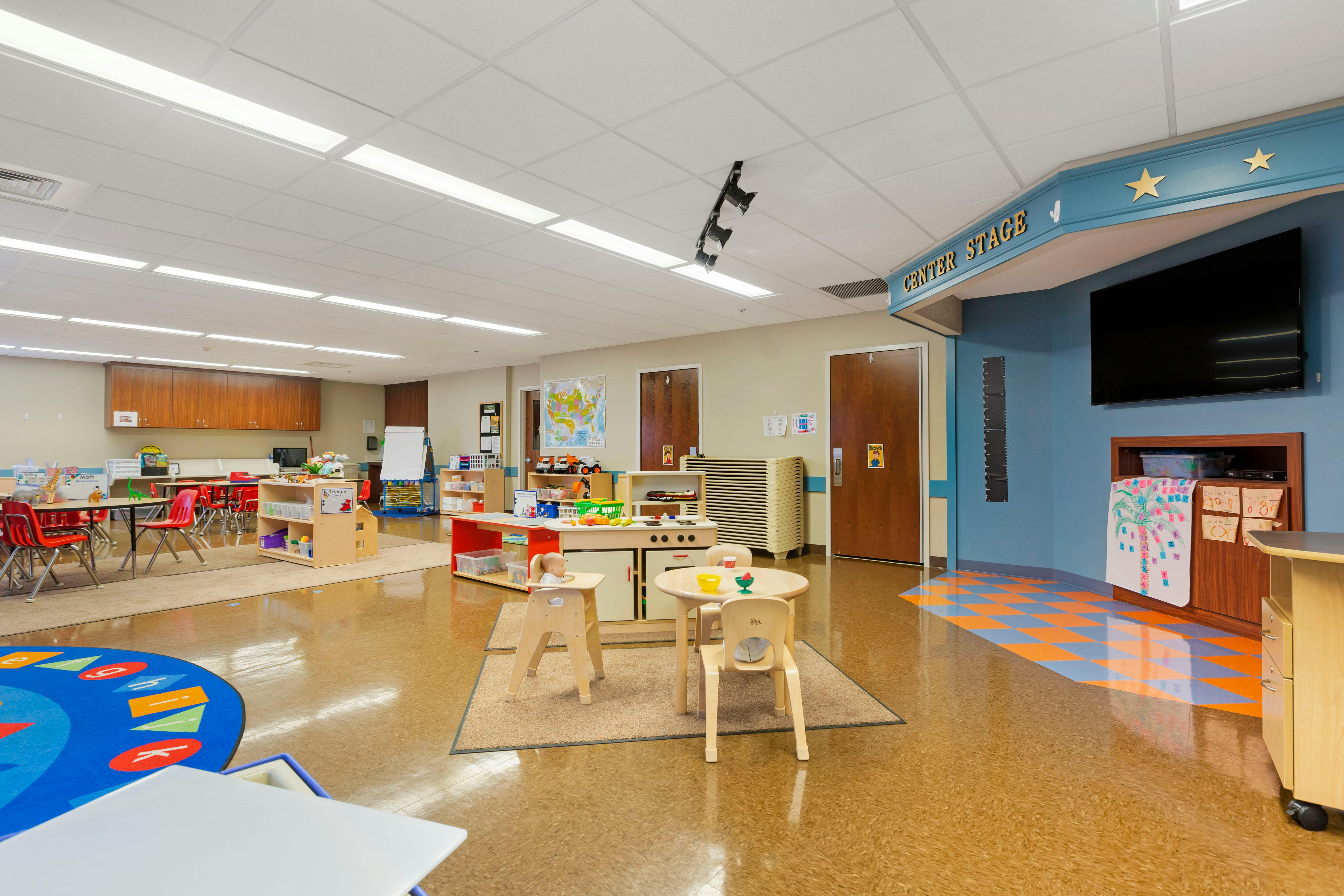 Classroom with child-sized tables and chairs, play kitchen, and "CENTER STAGE" sign