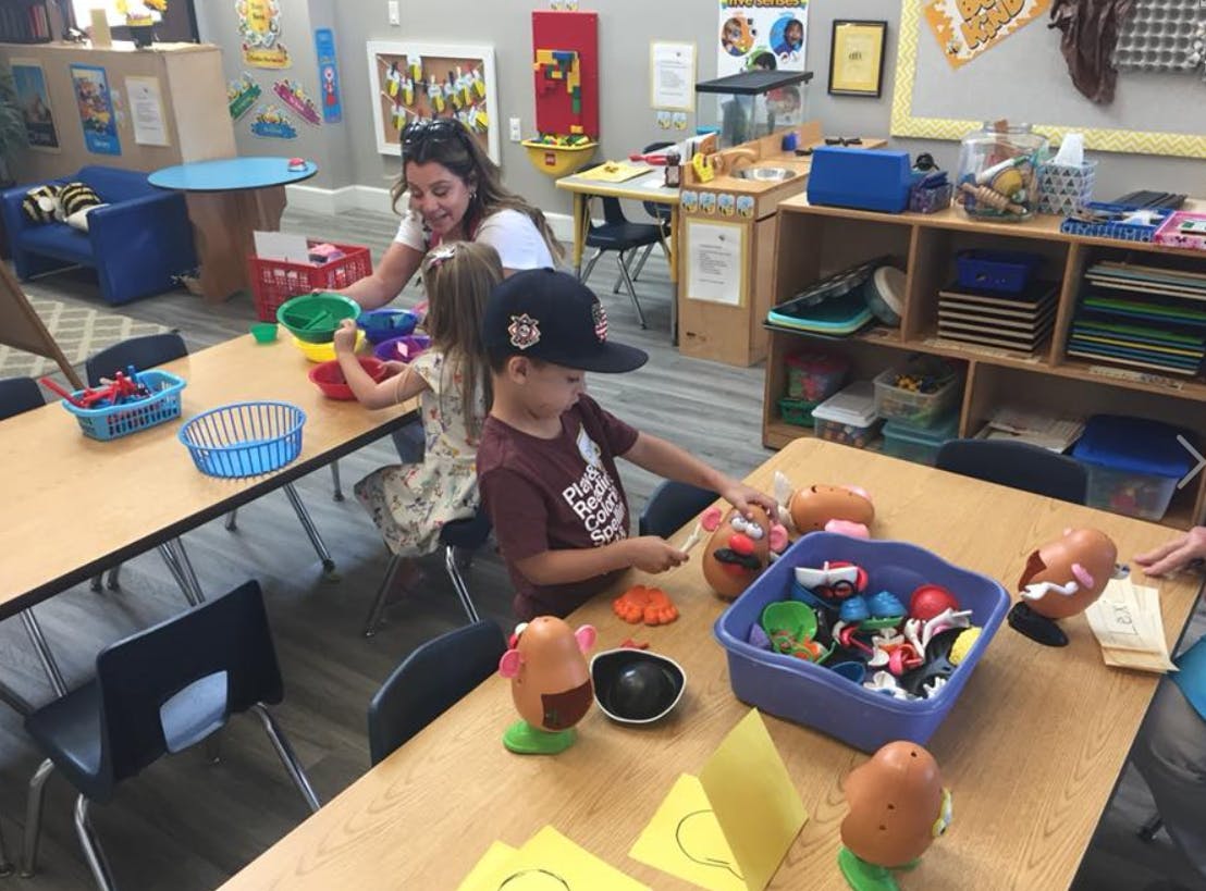 Adult and children playing with toys at tables in a classroom