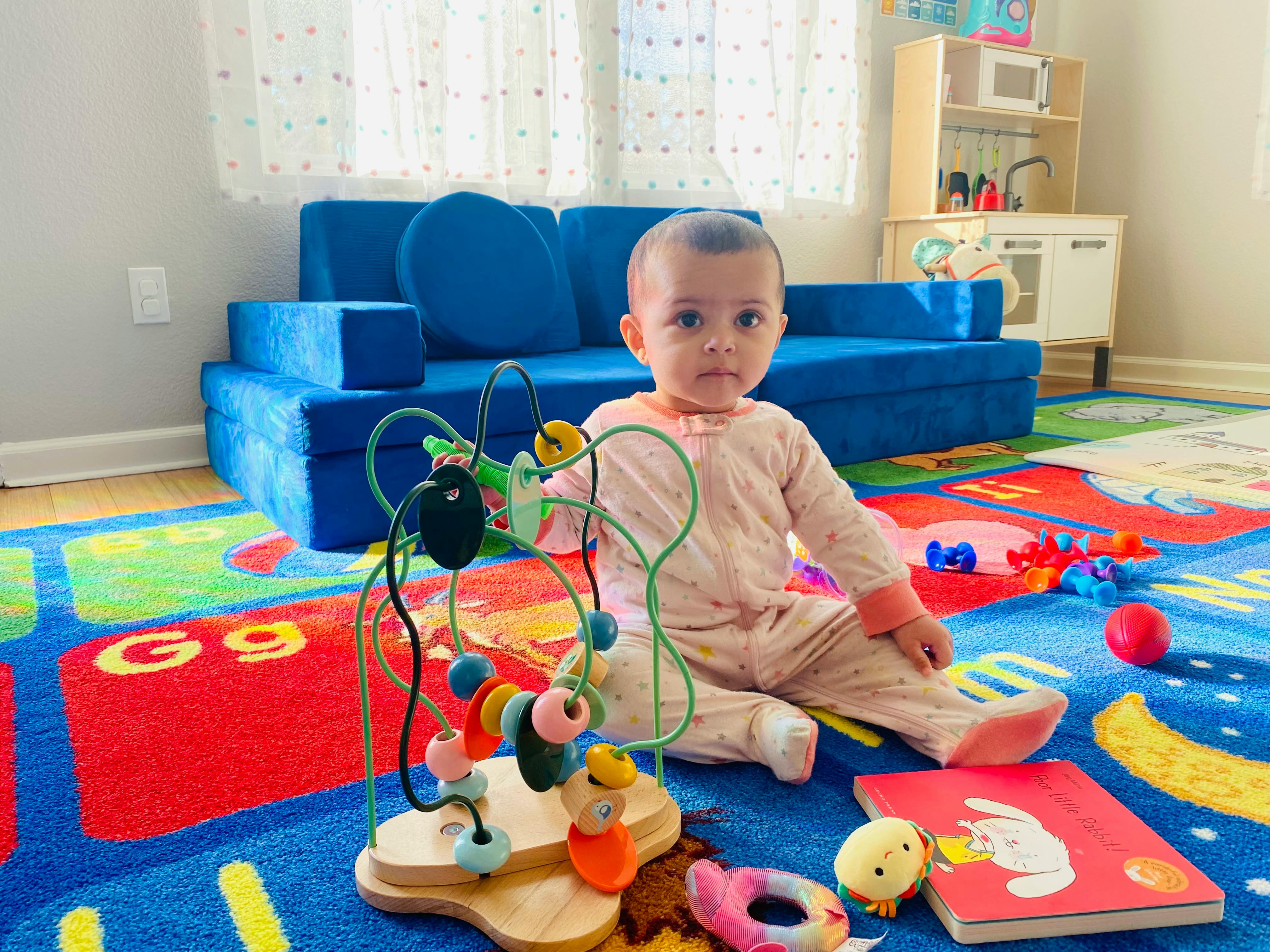 Child sitting on a colorful rug with a bead maze toy