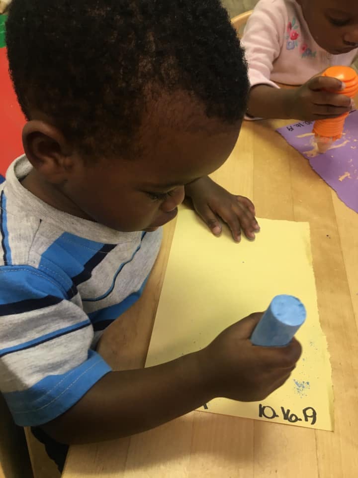Child drawing on paper with a blue crayon