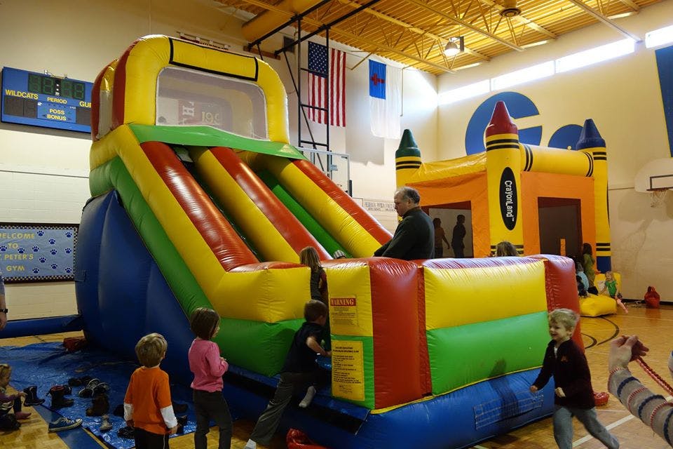People and children playing on colorful inflatable slides and bounce houses in a gym