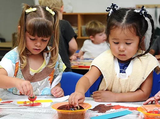 Two children painting at a table in a classroom