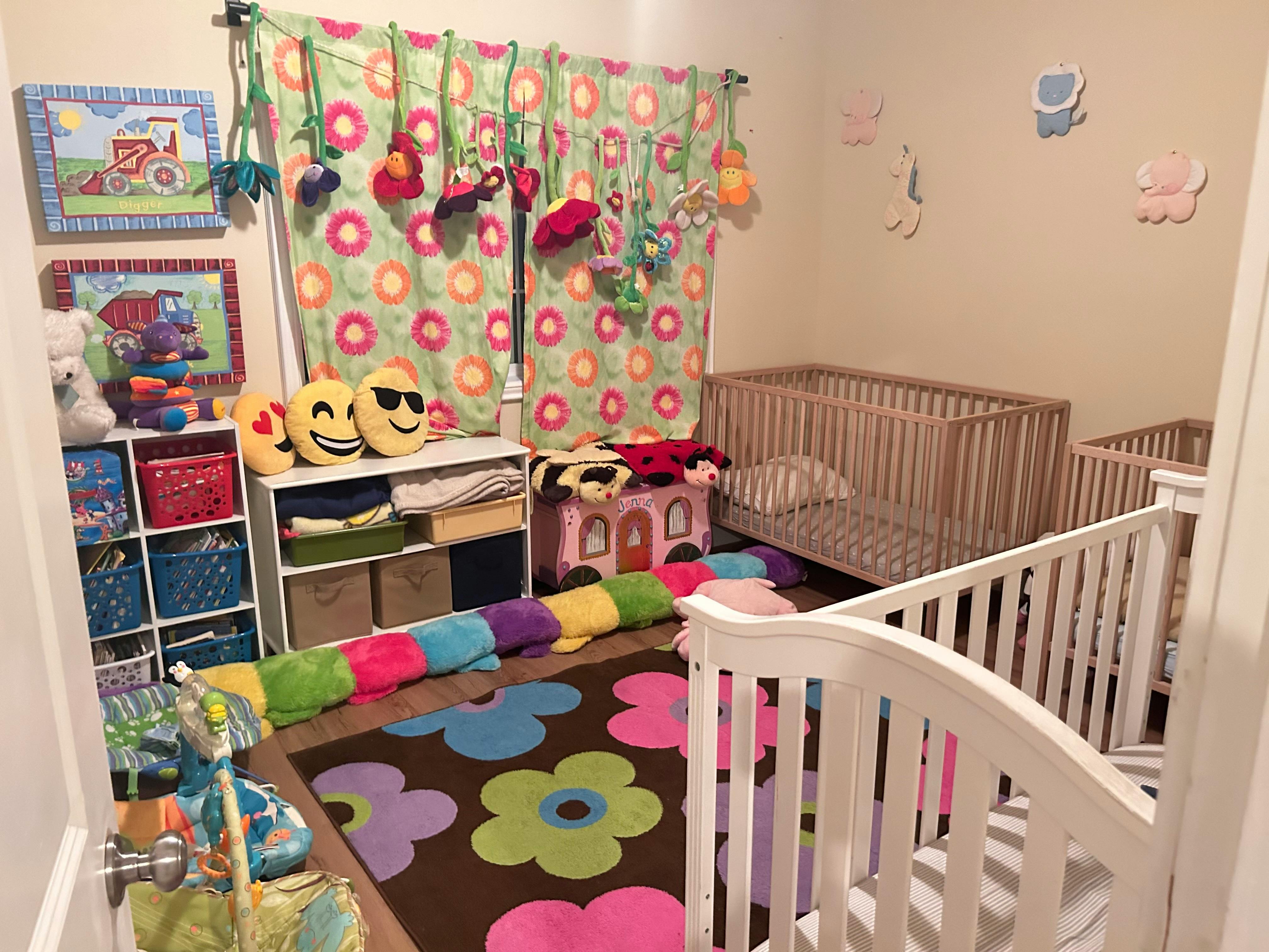 Nursery room with multiple cribs, colorful rug, and storage shelves