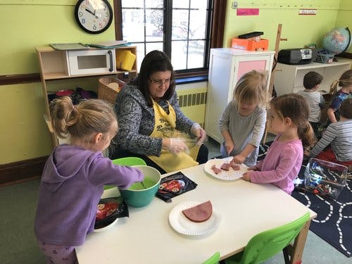 Adult and children preparing food at a table in a classroom