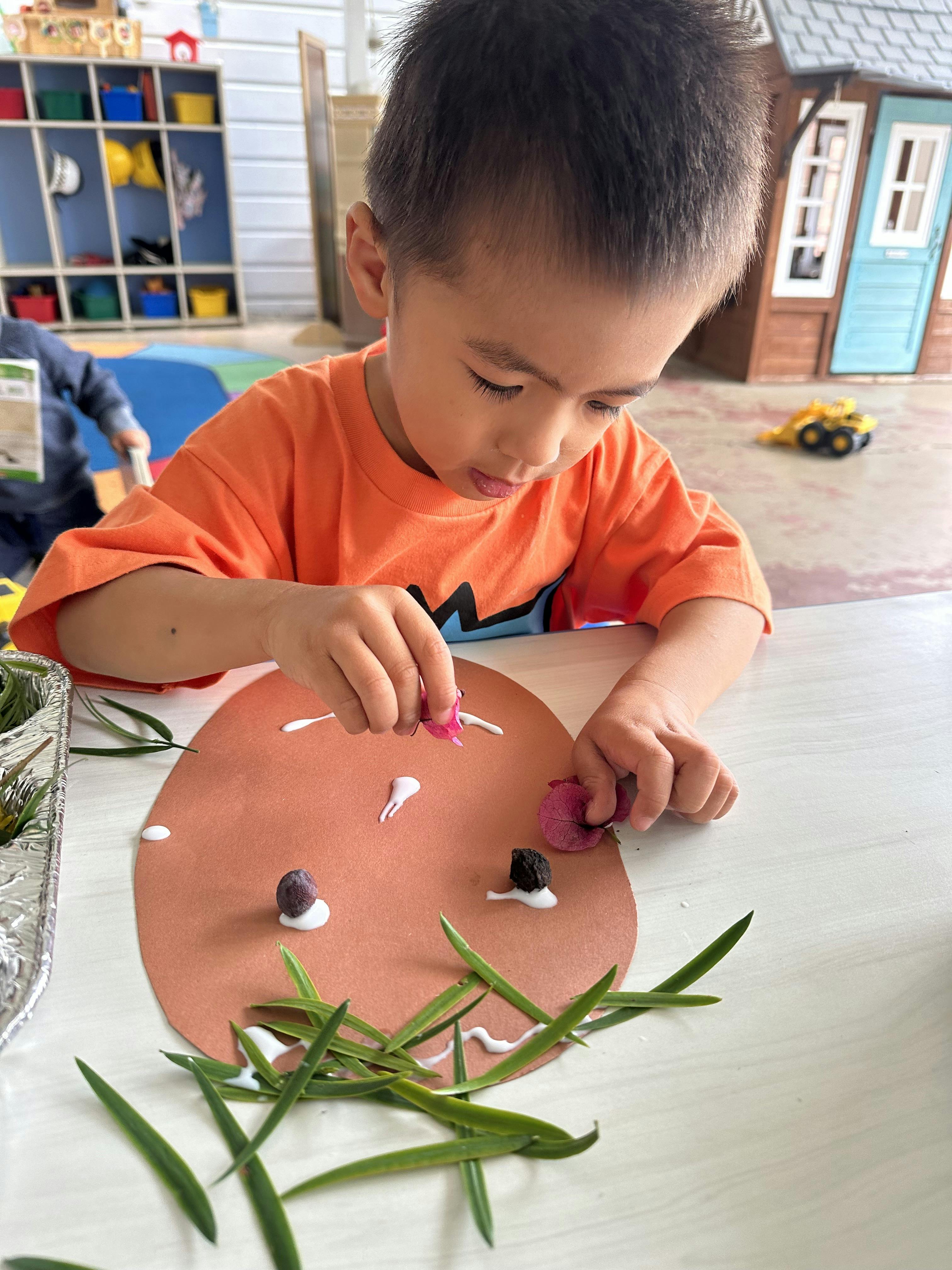 Child gluing natural elements onto a paper shape at a table