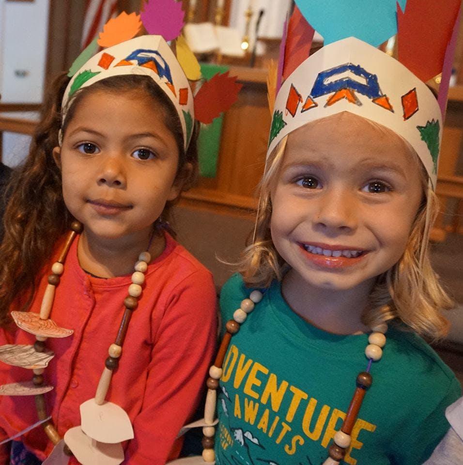 Two children wearing paper headbands and beaded necklaces
