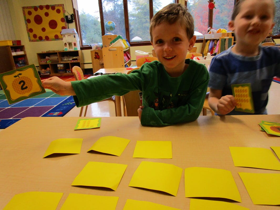 Child holding up a card with the number 2, another child nearby