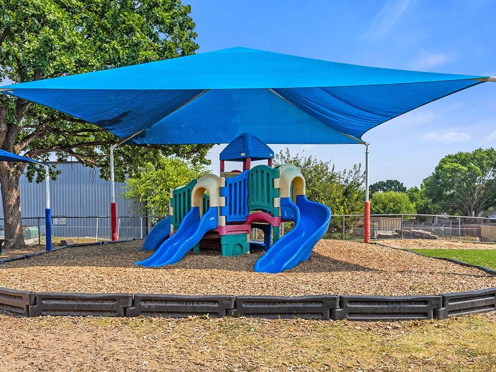 A colorful playground with slides under a blue sun shade