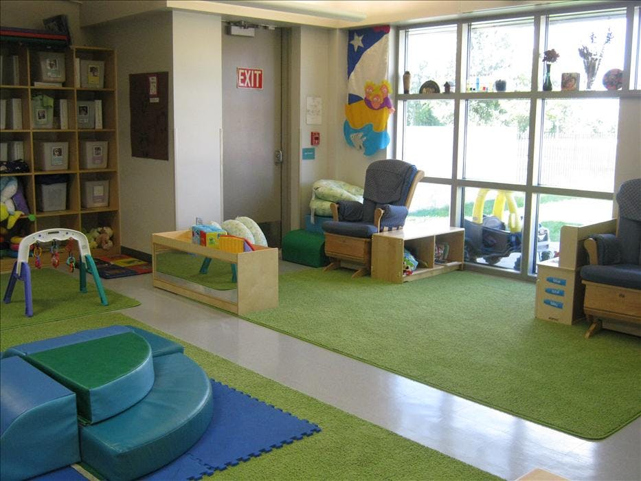 Childcare classroom with green rugs, play equipment, and an exit sign