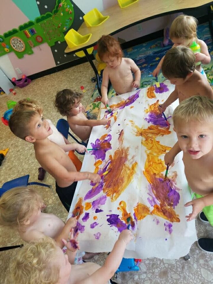 Multiple children painting on a large sheet of paper
