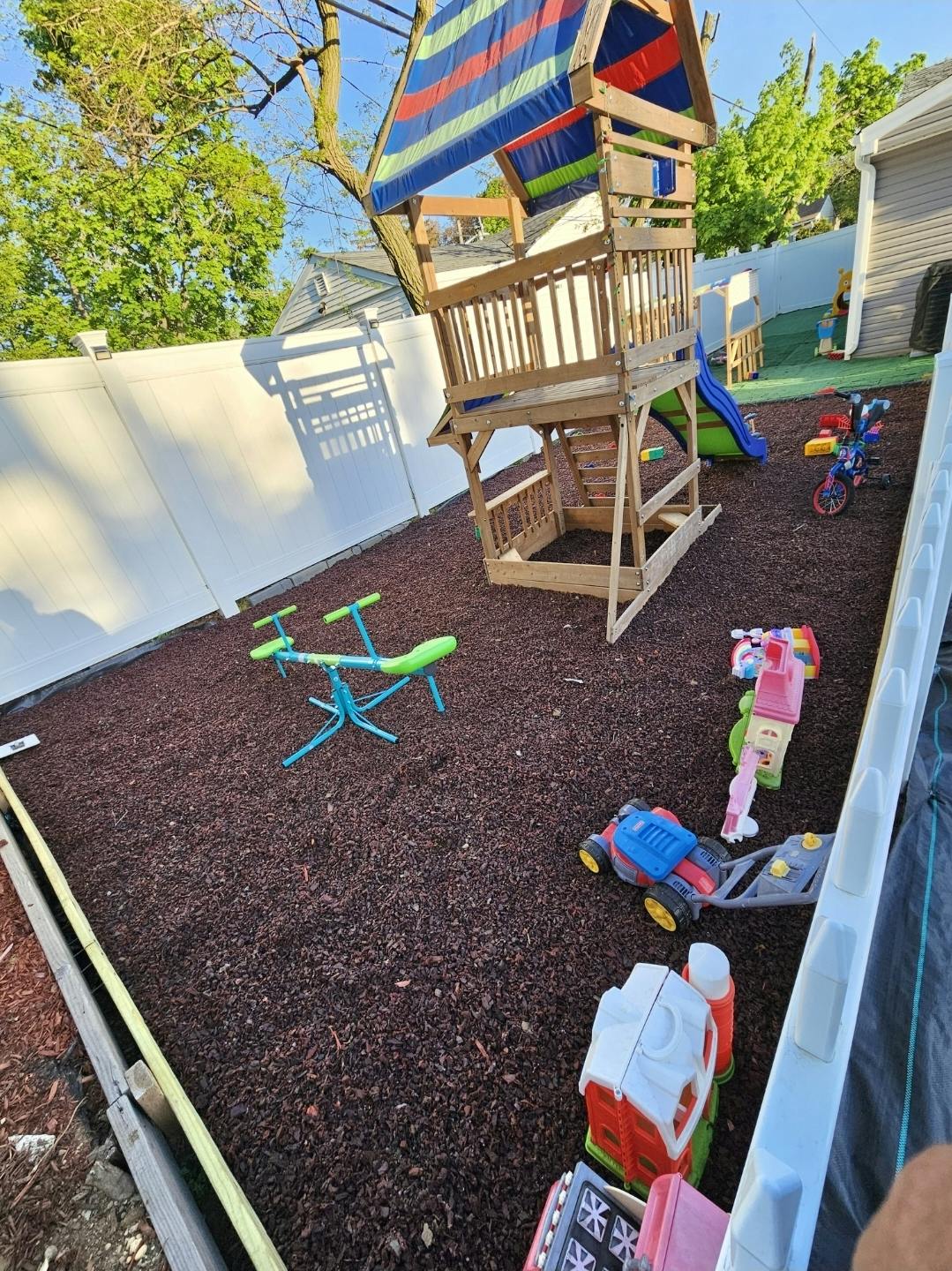Outdoor playground with a wooden playset, slide, seesaw, and toys on mulch