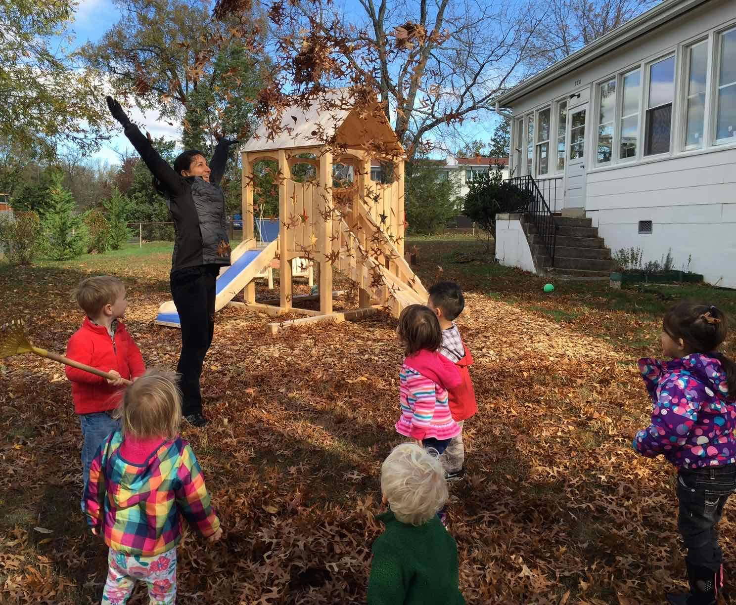 Person throwing leaves in the air with children watching in a yard