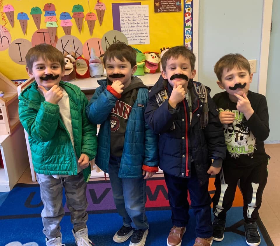 Four children with fake mustaches in a classroom