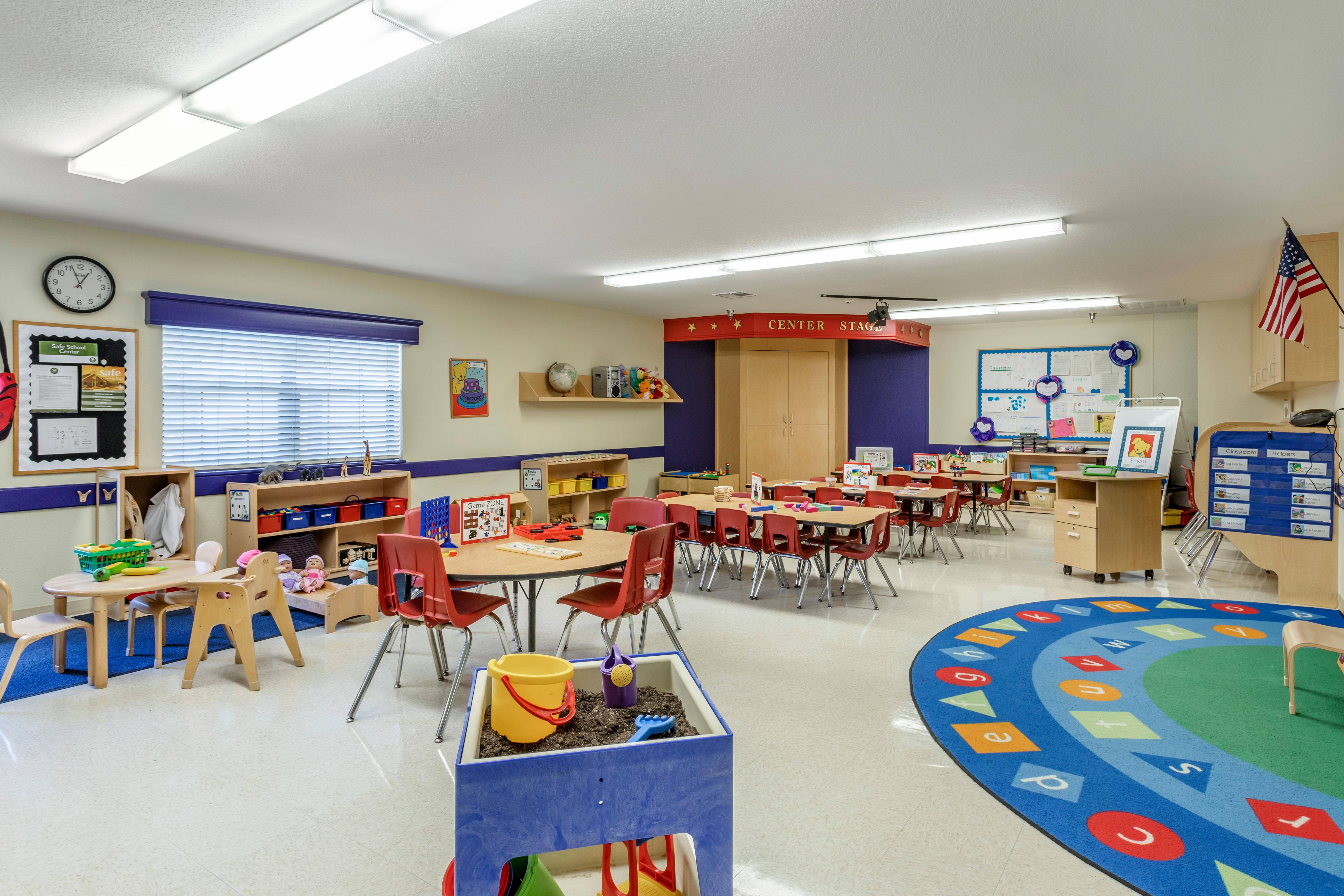 Classroom with small tables and chairs, a sand table, and an alphabet rug