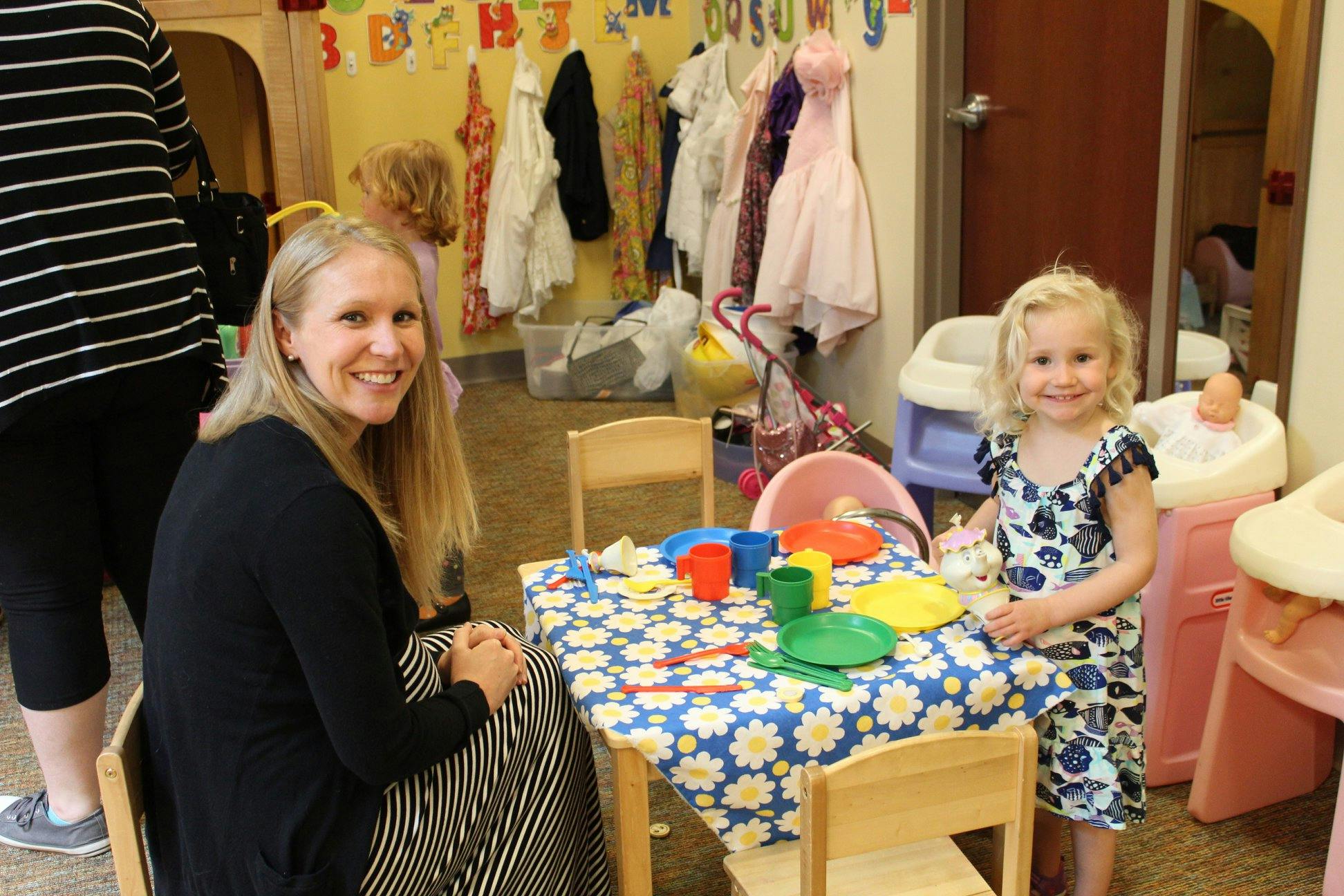 Person and child at a small table with play dishes