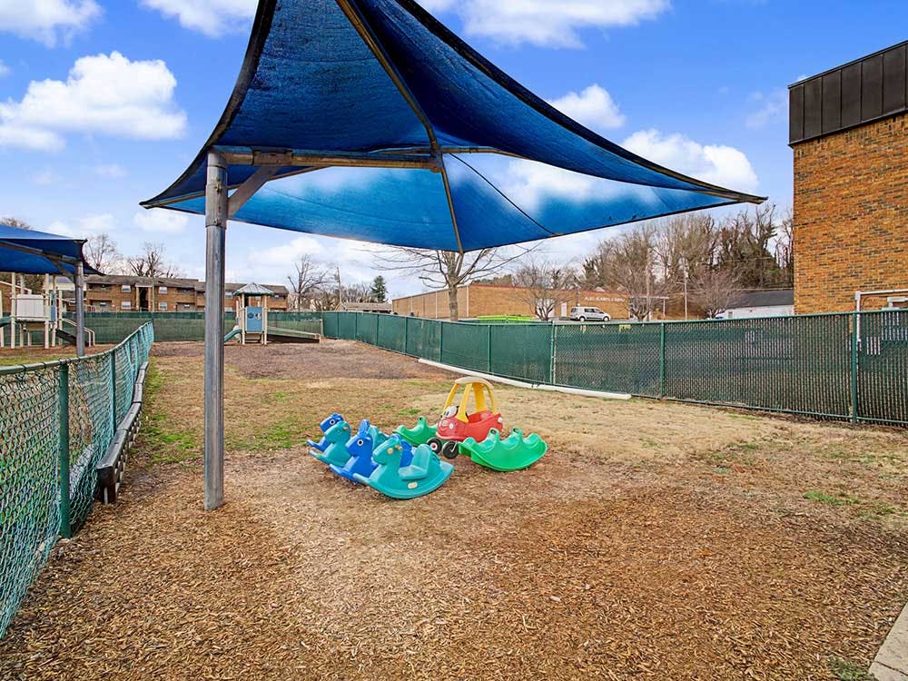 A covered outdoor play area with rocking toys and a distant playground