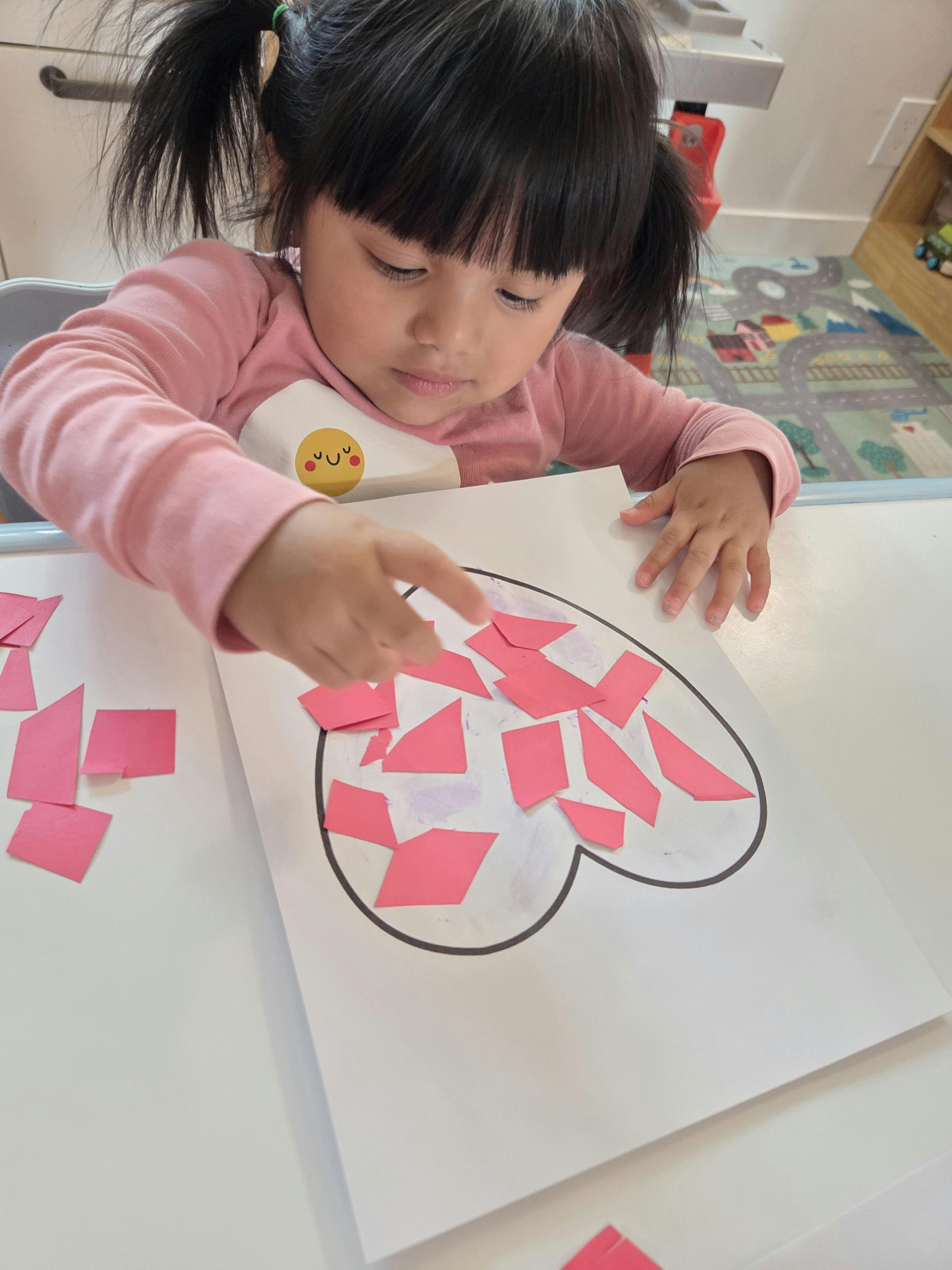 Child gluing paper pieces onto a heart drawing