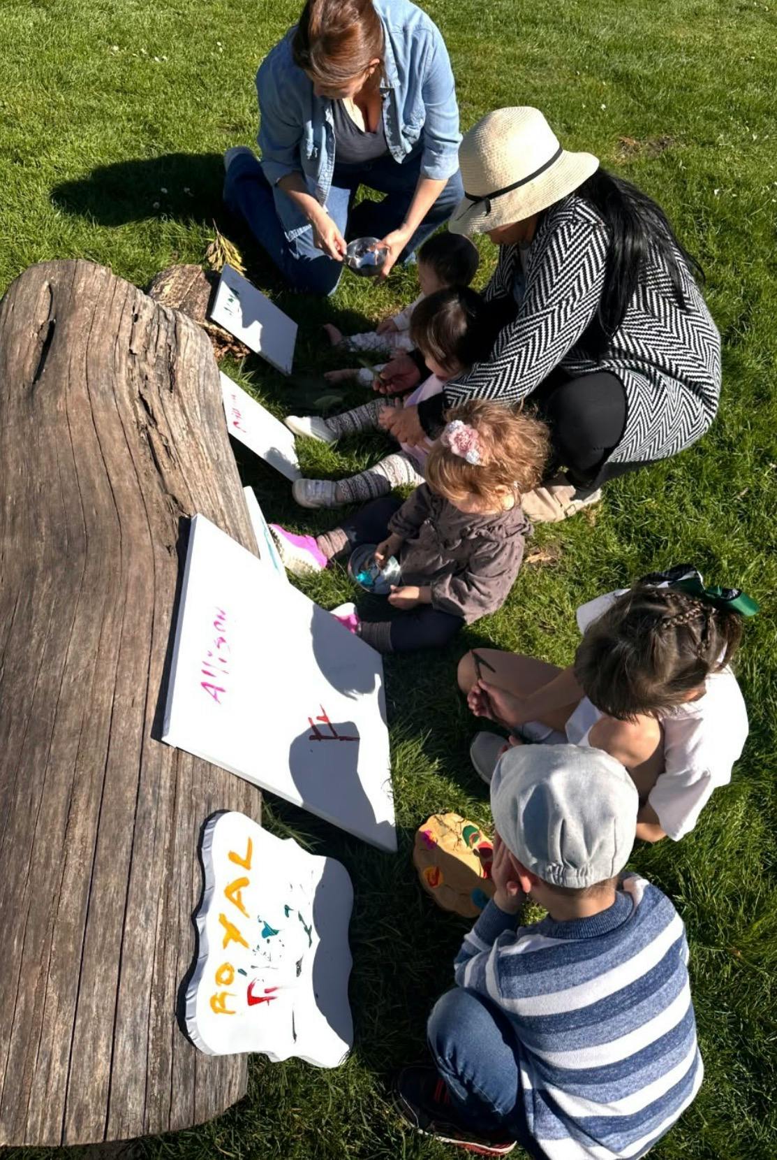 People sitting on grass painting on canvases next to a log