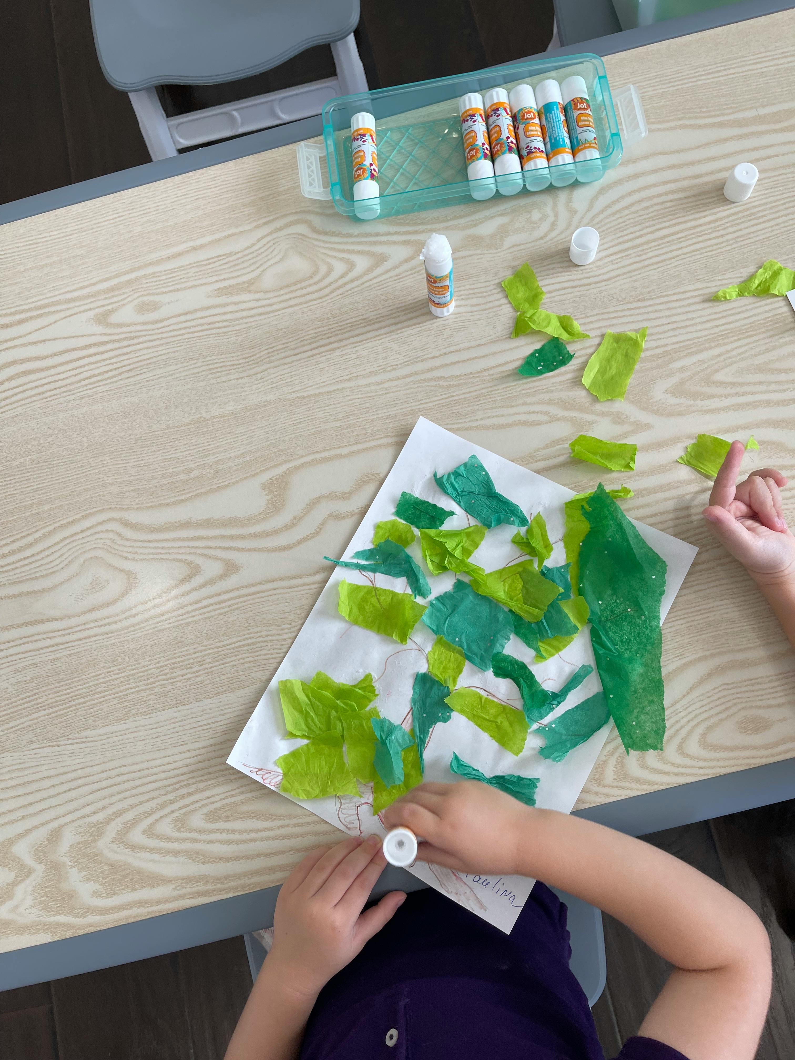 Child gluing green paper scraps onto paper at a table