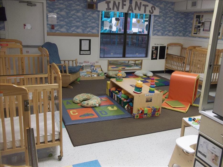 An infant room with multiple cribs, a rocking chair, and a play area
