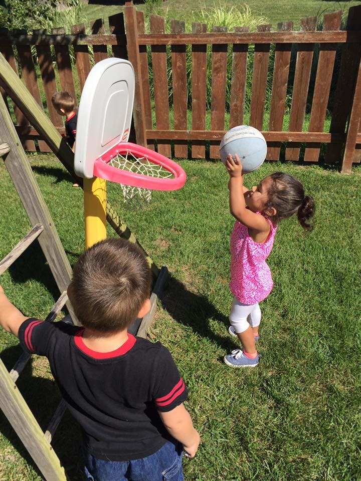 Child holding a basketball up to a hoop, another child in foreground