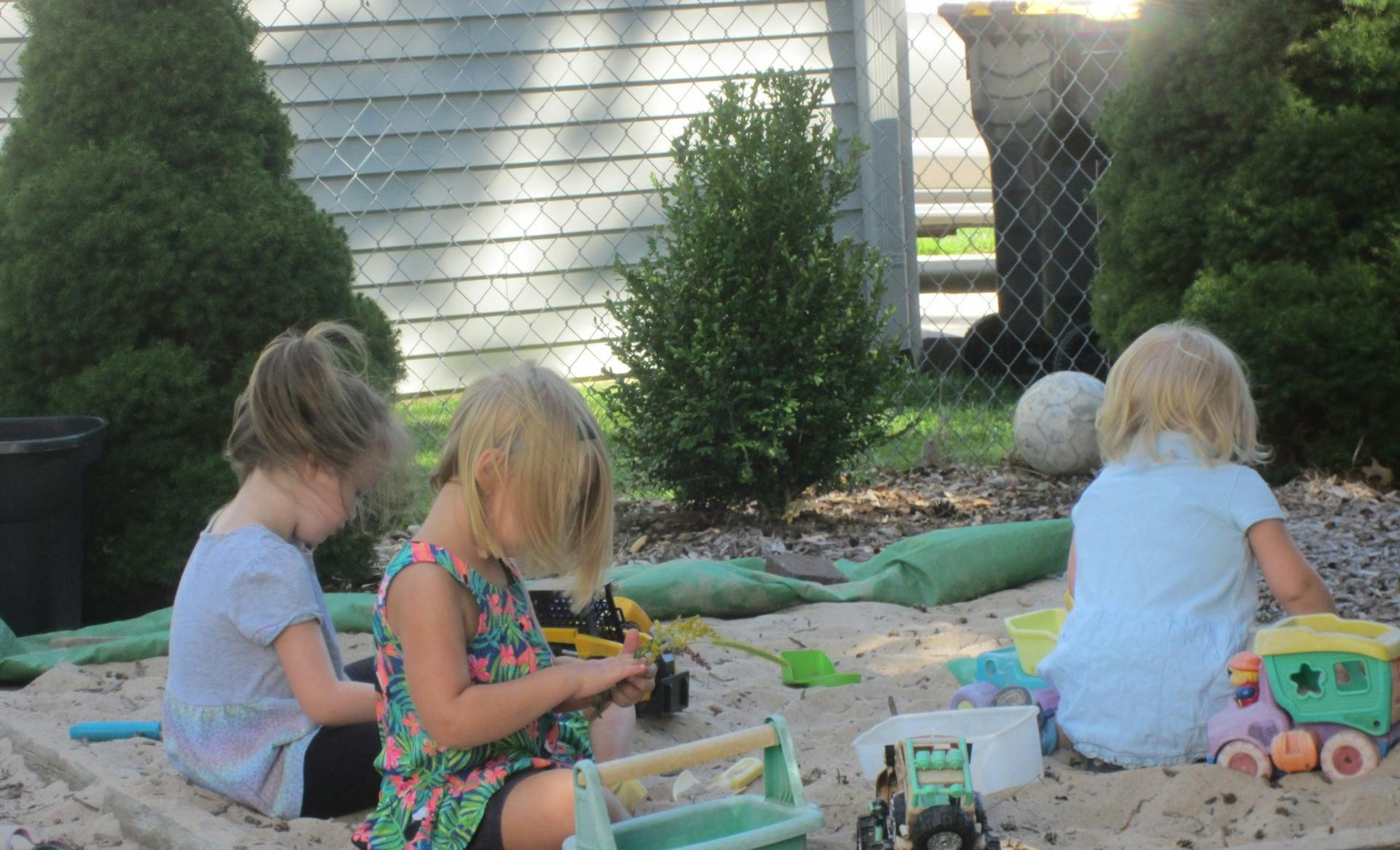 Three children playing in a sandbox with toys