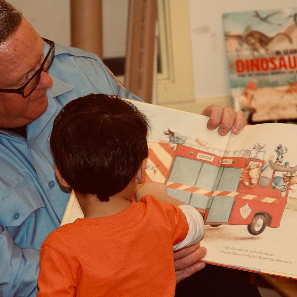 Adult and child reading a book with a fire truck illustration