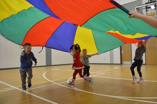 Children playing with a colorful parachute indoors