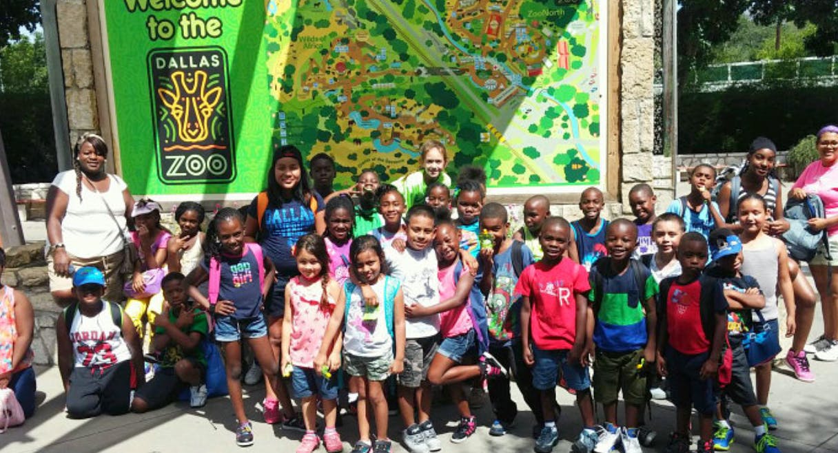 Group of children and adults posing in front of a Dallas Zoo sign