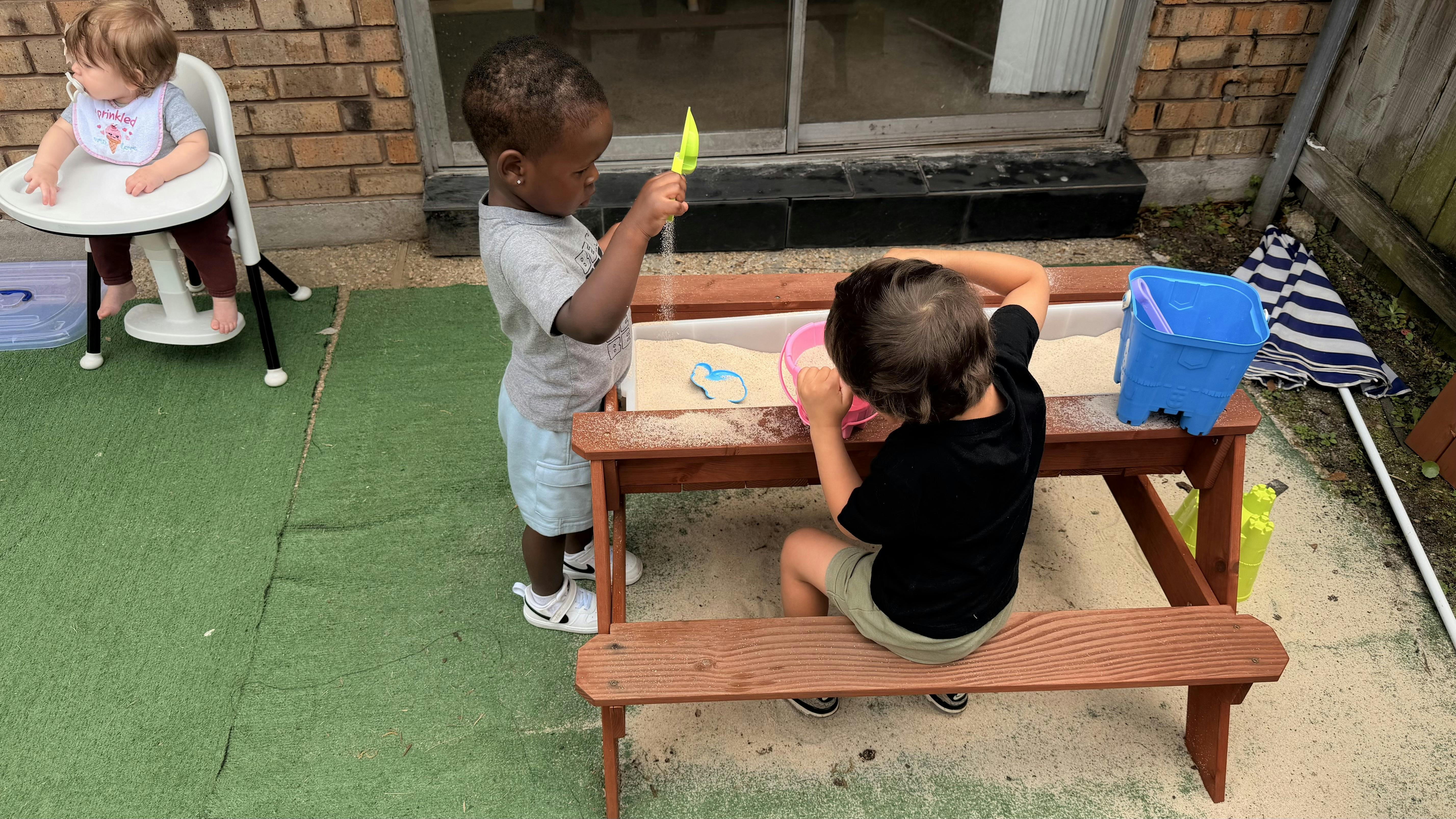 Two children playing with sand at a small wooden table outdoors