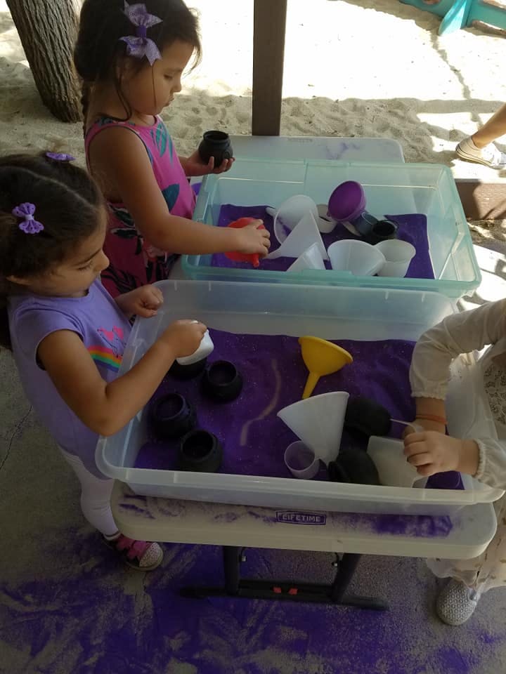 Children playing with purple sand and funnels in sensory bins