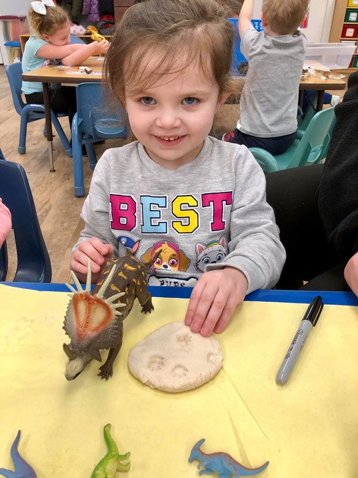 Child playing with dinosaur toys and clay in a classroom