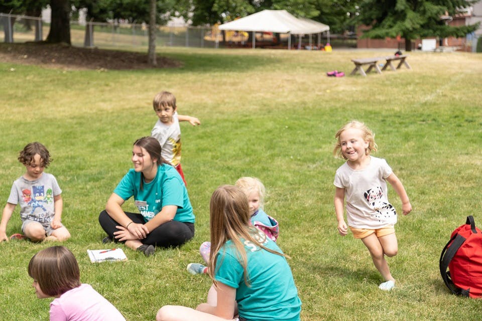 Adults and children sitting and playing on grass