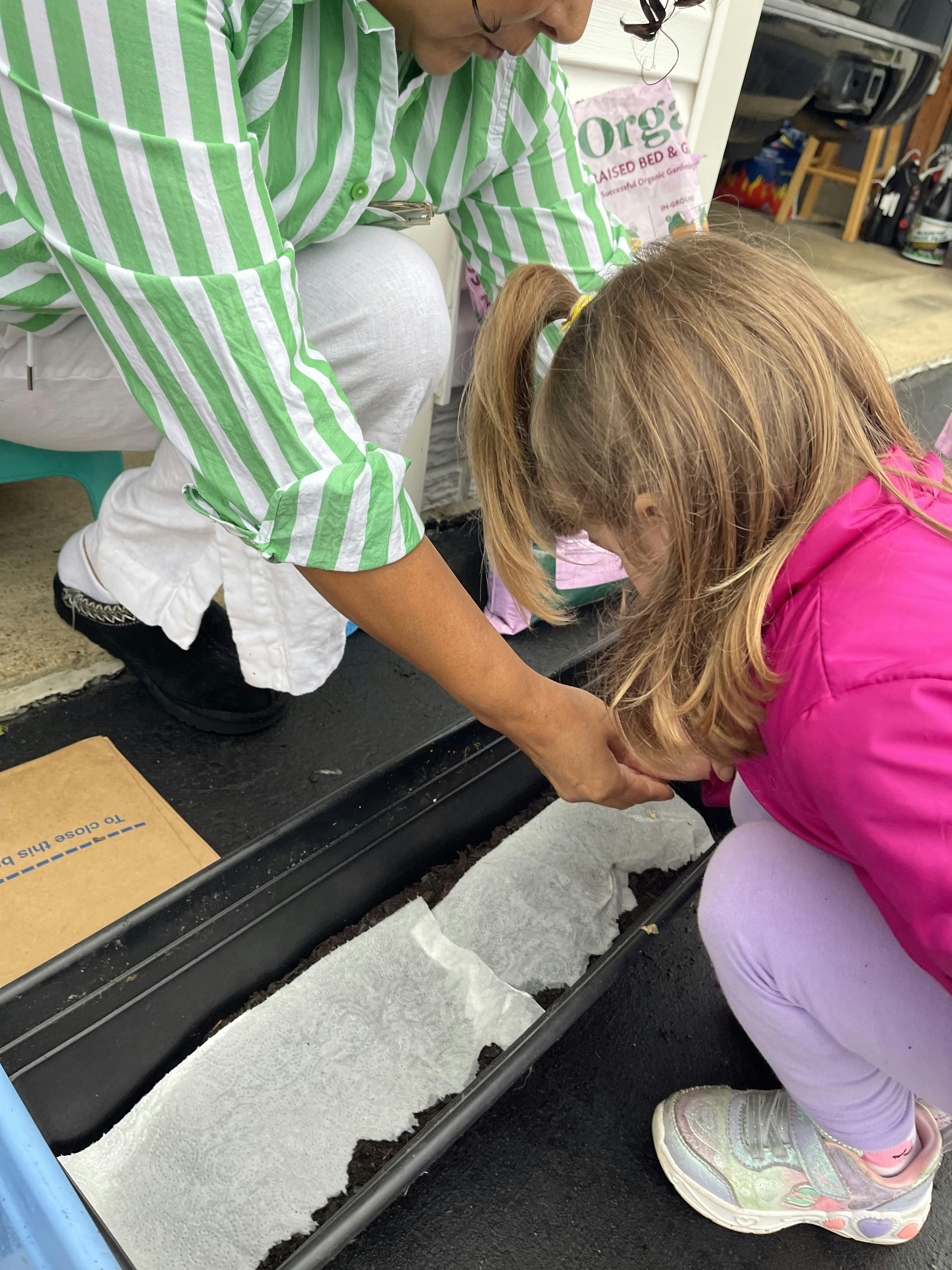 A person and a child planting seeds in a garden planter