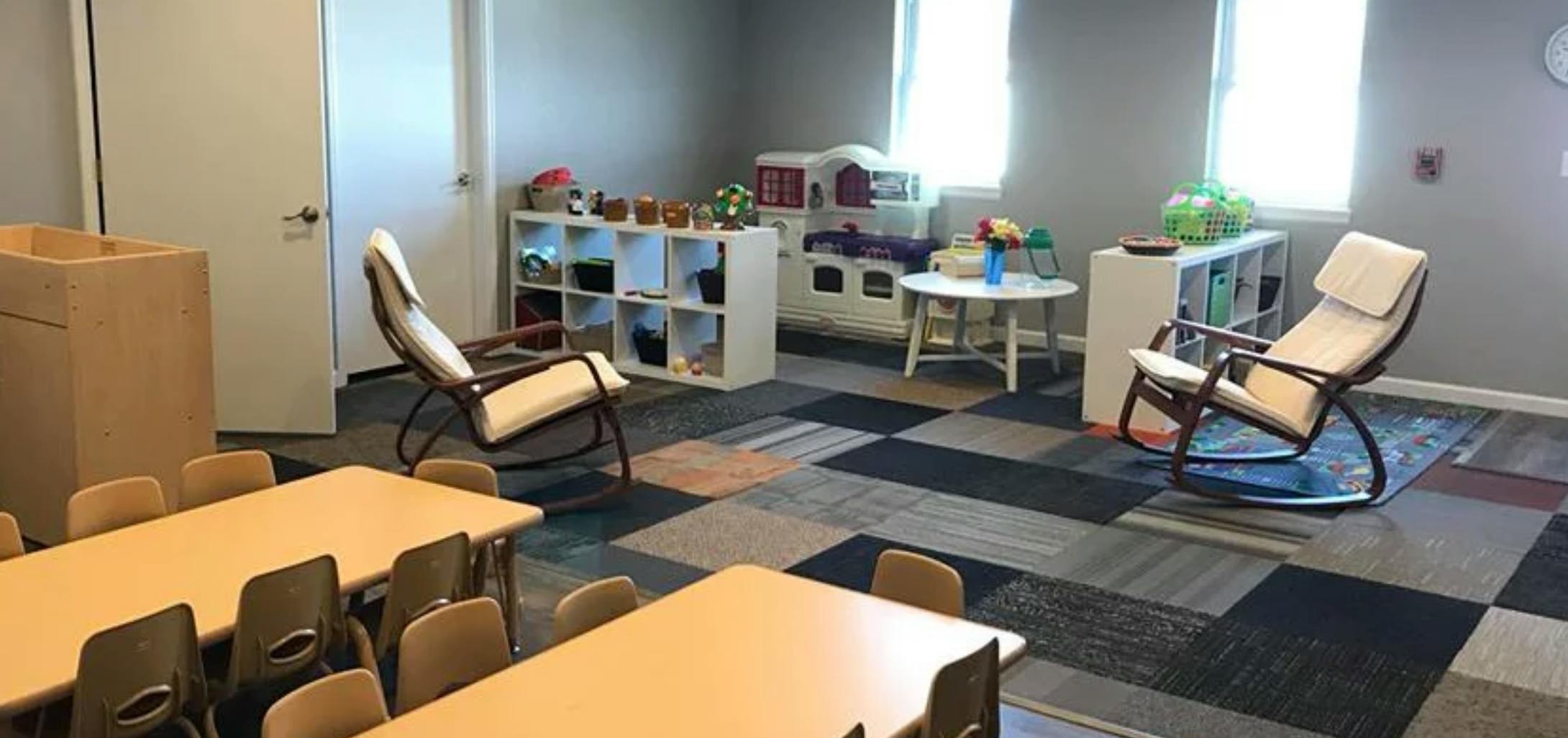 Classroom with small tables and chairs, rocking chairs, and storage shelves