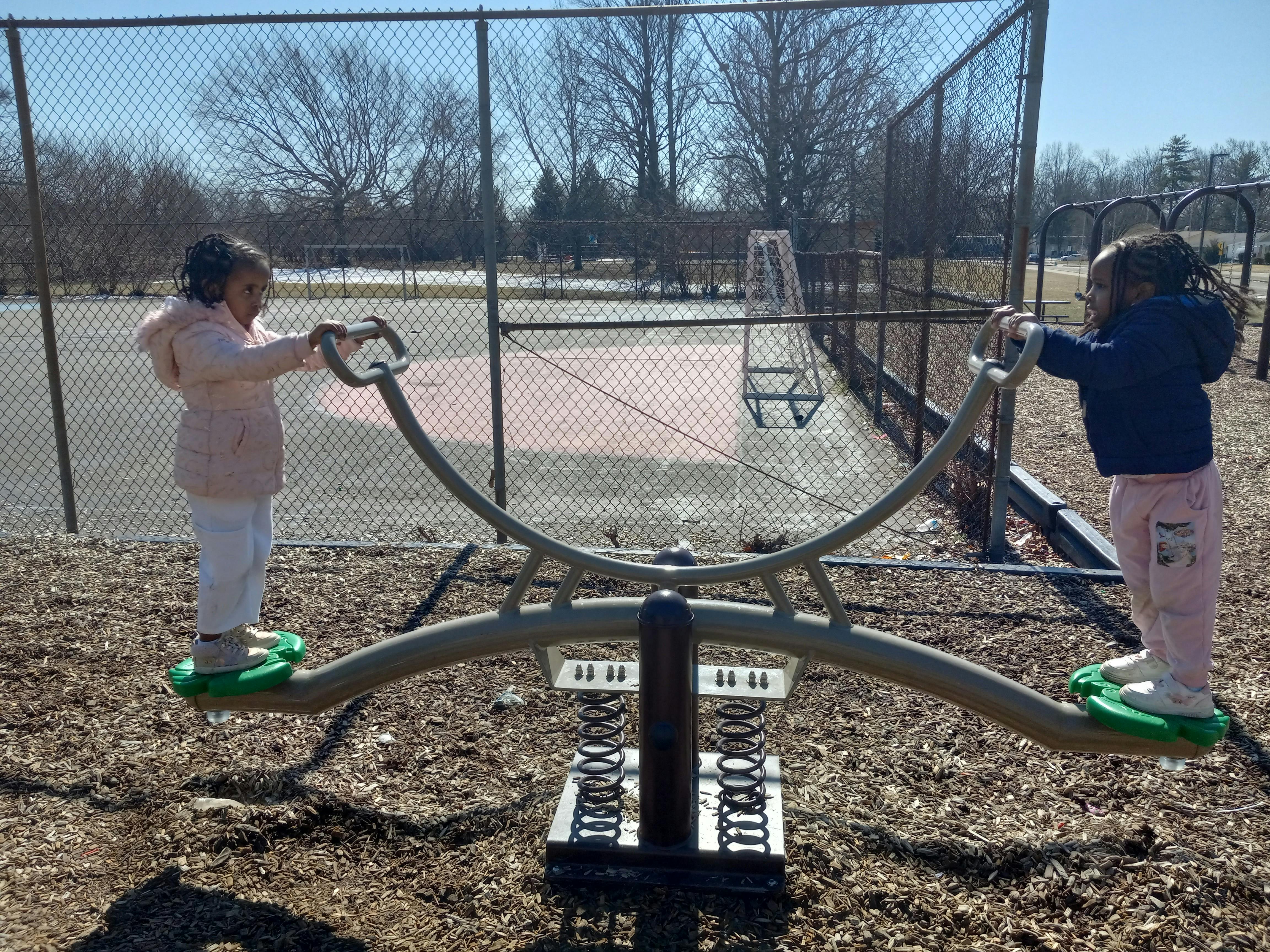 Two children standing on a seesaw at a playground