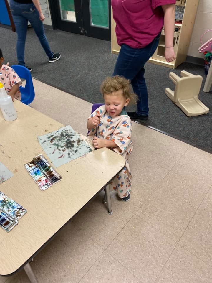 Child sitting at a table with paint and paper